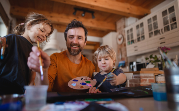 A mature father with two small children resting indoors at home, painting pictures.