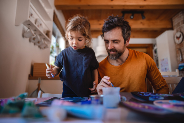 A mature father with small daughter resting indoors at home, painting pictures.