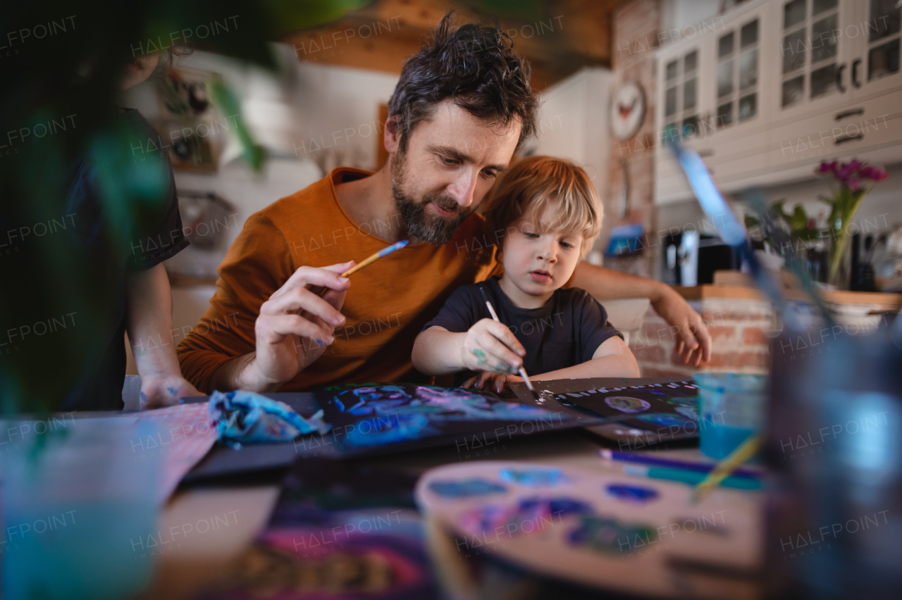 A mature father with two small children resting indoors at home, painting pictures.