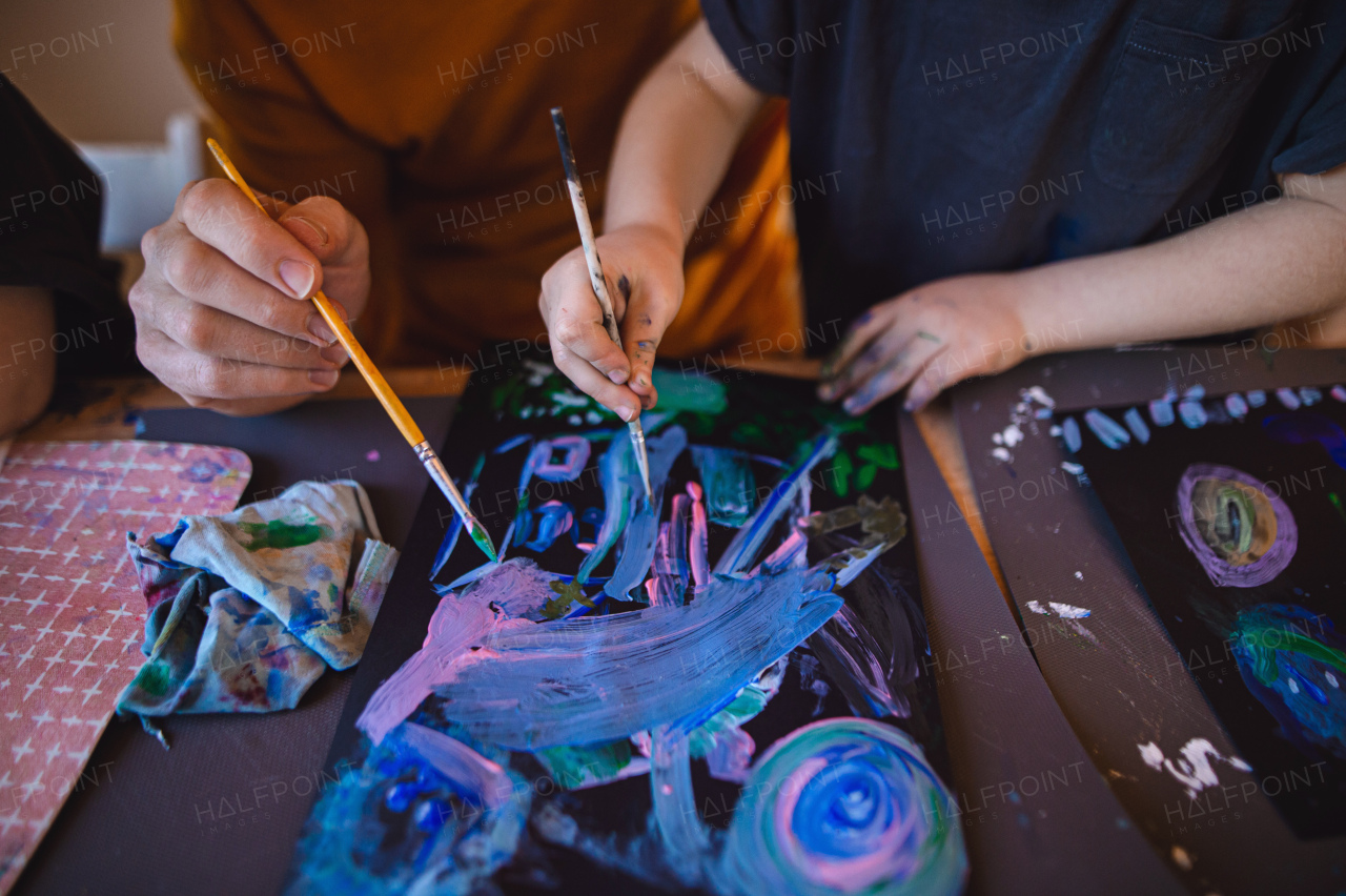 A high angle view of unrecognizable father with small child painting pictures indoors at home.