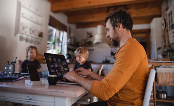 Mid-adult father with two small children working indoors at home, painting pictures and home office concept.