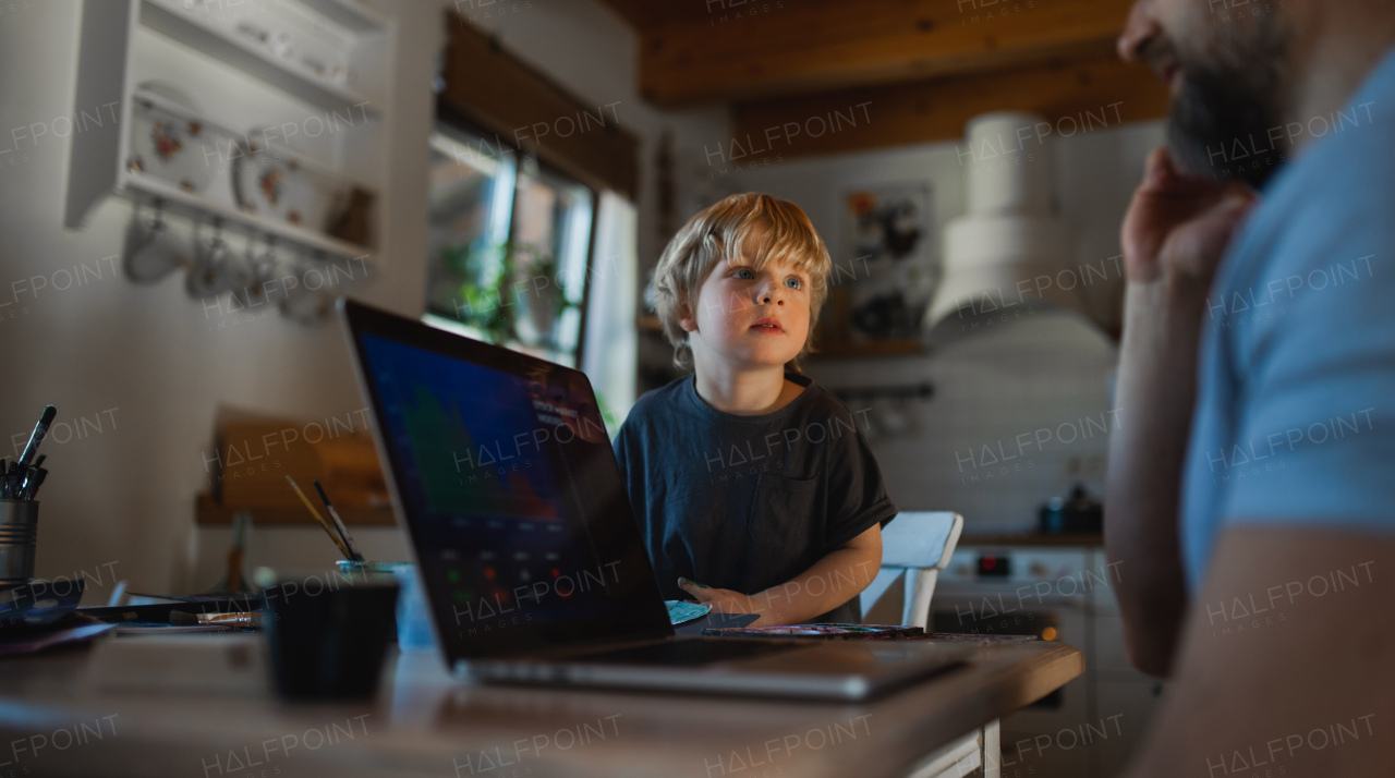 An unrecognizable father with small son working indoors at home, painting pictures and home office concept.