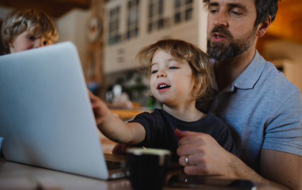 A mid adult father with small children working indoors at home, home office concept.