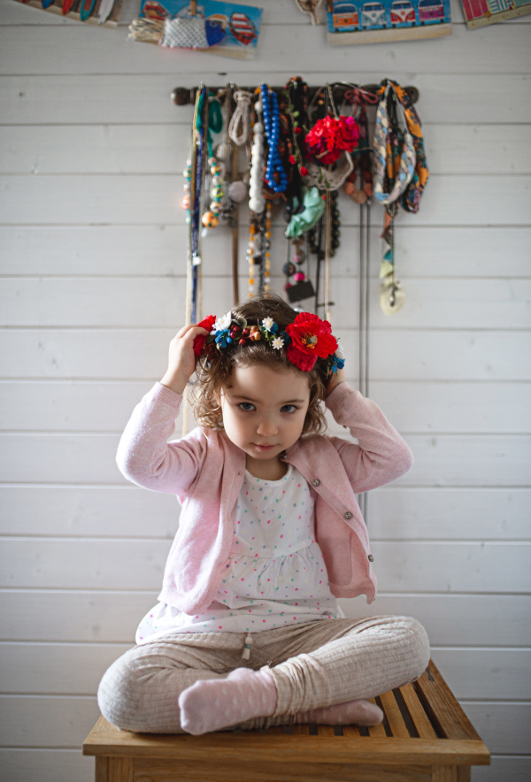 A portrait of little girl with folk flower crown sitting indoors at home