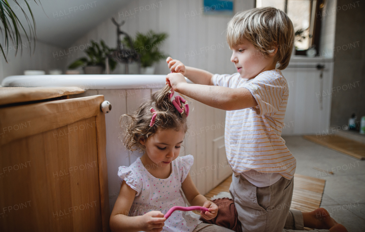 A little boy applying hair culers hair curlers to his little sister indoors at bathroom.