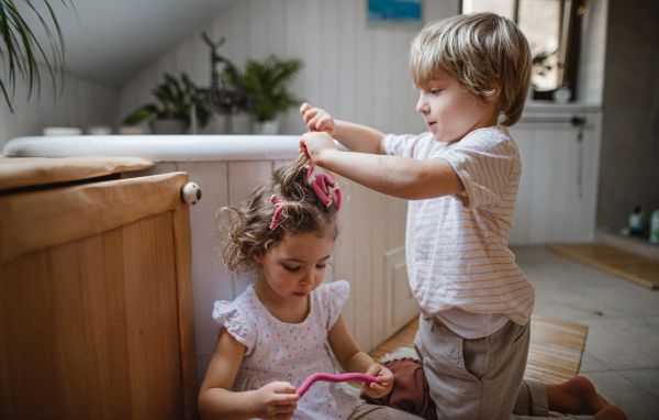 A little boy applying hair culers hair curlers to his little sister indoors at bathroom.