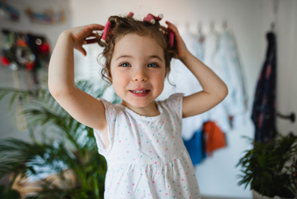 A portrait of small girl with hair curlers indoors at home, looking at camera.