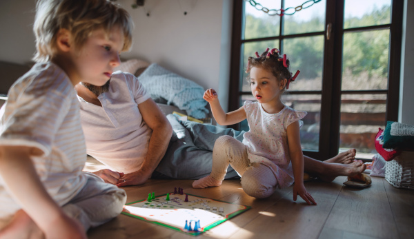 An unrecognizable father with two small children resting indoors at home, playing board game.