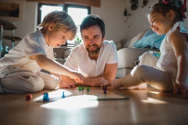 A mature father with two small children resting indoors at home, playing board games.