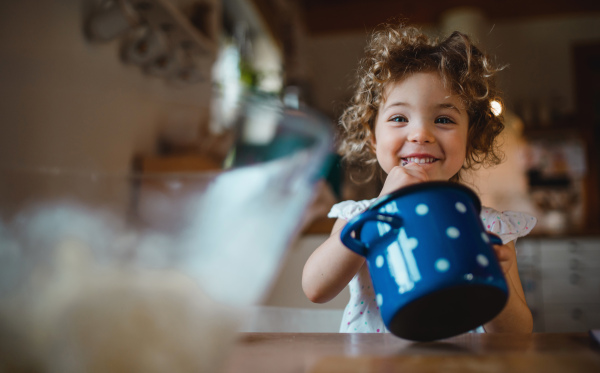 A happy small girl sitting at table indoors at home, eating spaghetti and looking at camera.