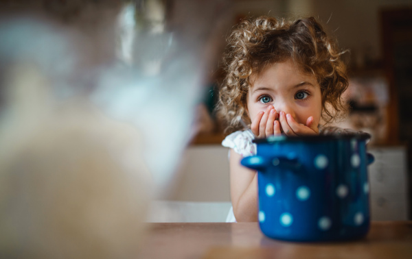 A happy small girl sitting at table indoors at home, eating spaghetti and looking at camera.