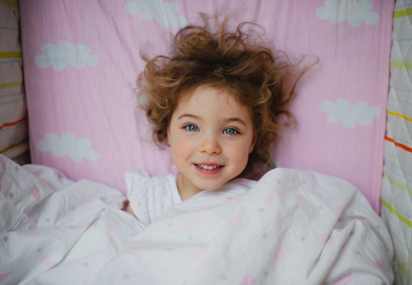 A top view of happy little girl lying in bed indoors at home