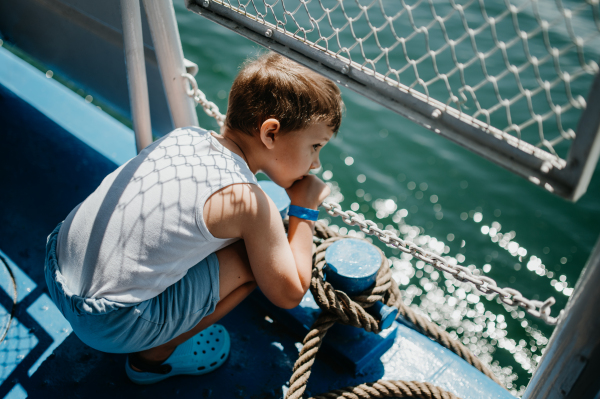 A little curious boy looking at water from motor boat.