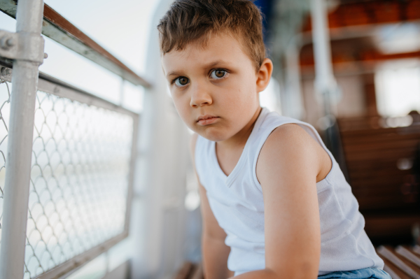 A little curious boy on summer cruise on sea with motor boat looking at camera.