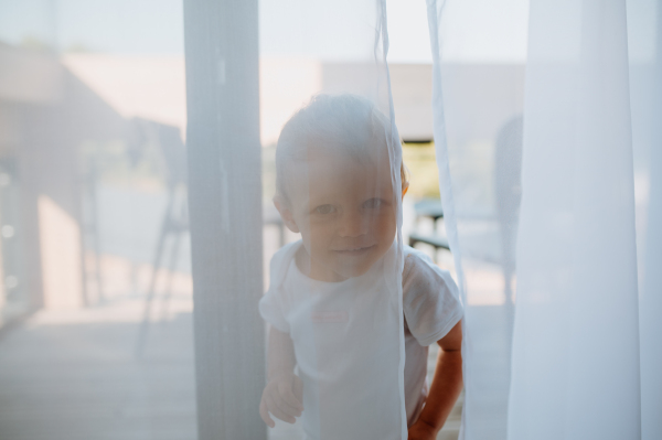 A cute baby girl playing,hiding behind curtains at home.