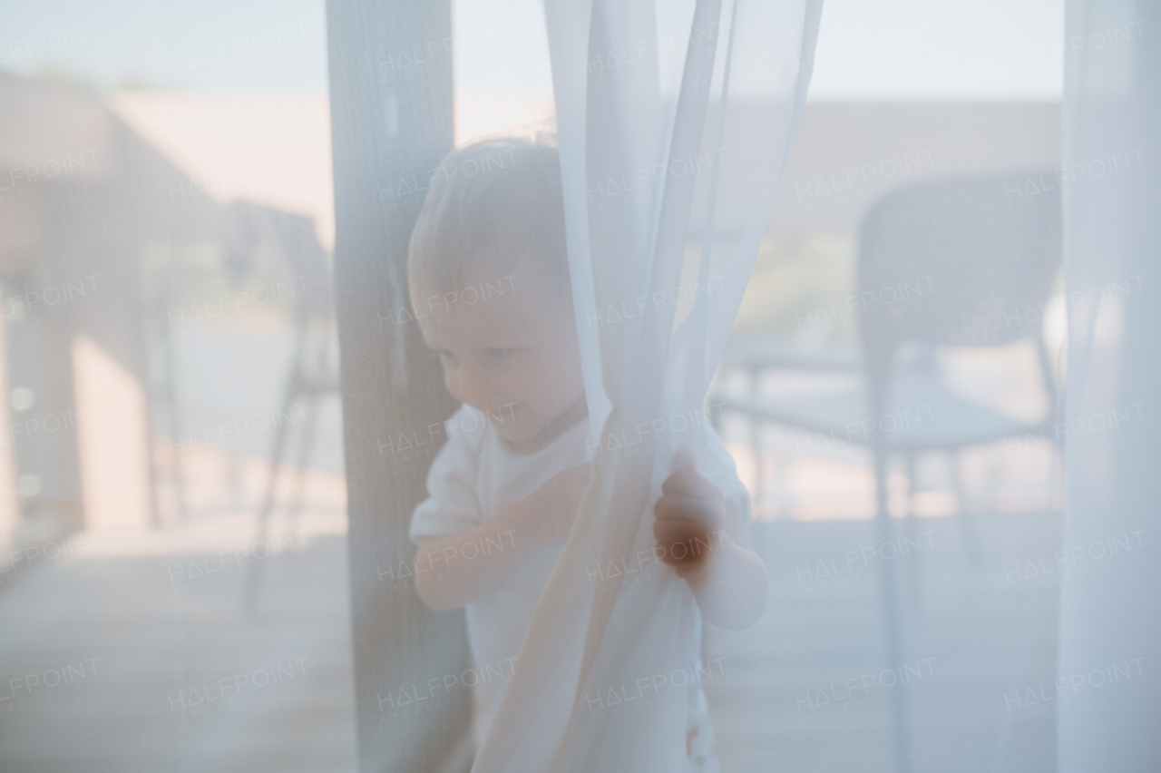 A cute baby girl playing,hiding behind curtains at home.