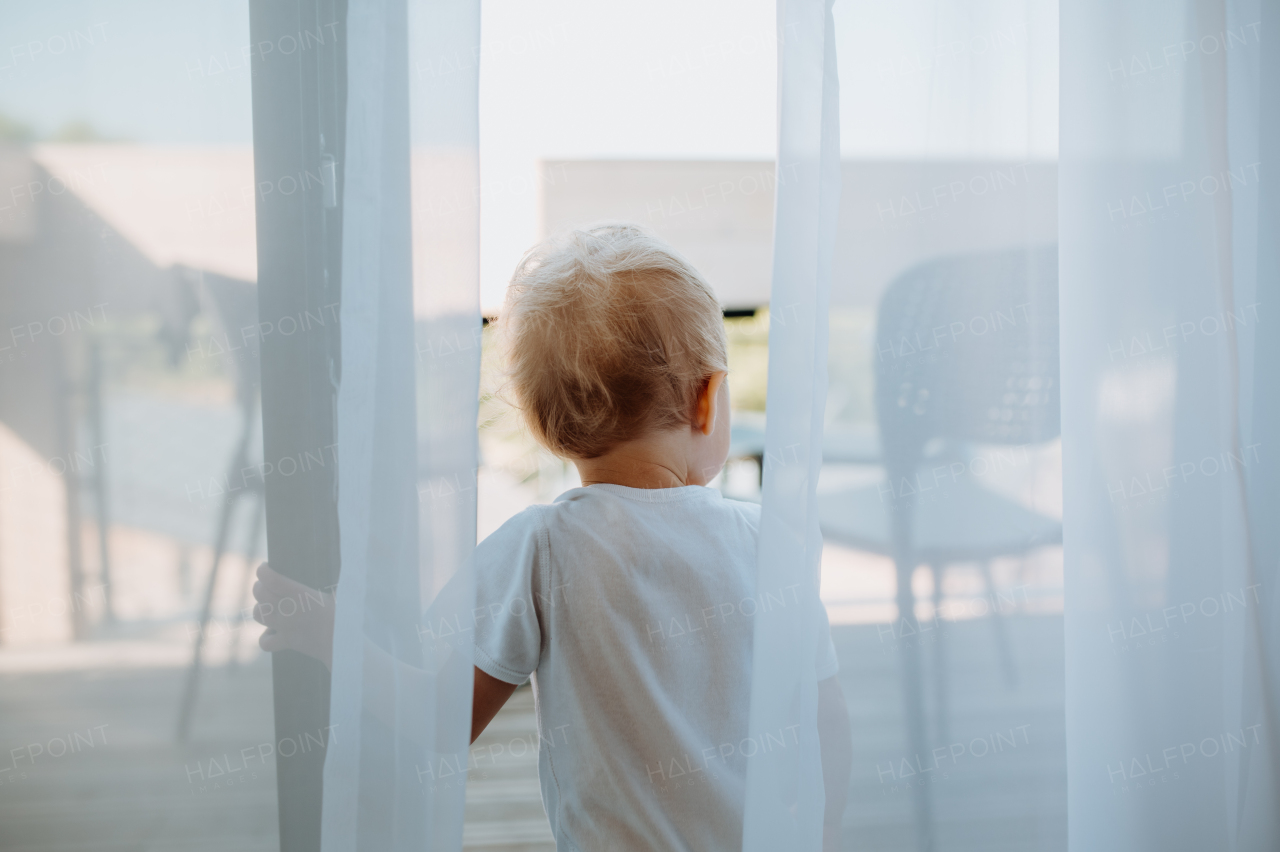 A cute baby girl playing,hiding behind curtains at home.