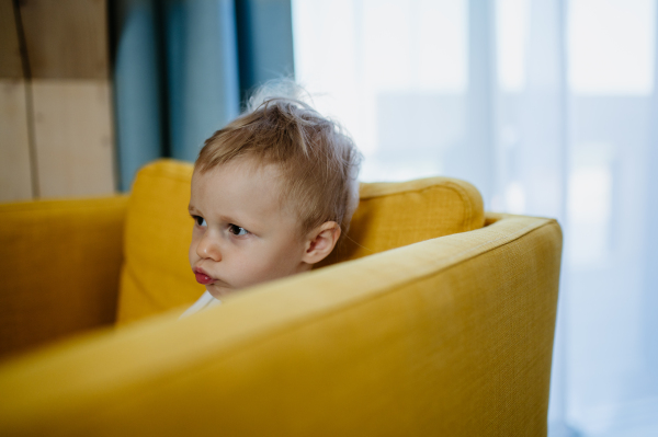 A little curious girl sitting on sofa and looking away.