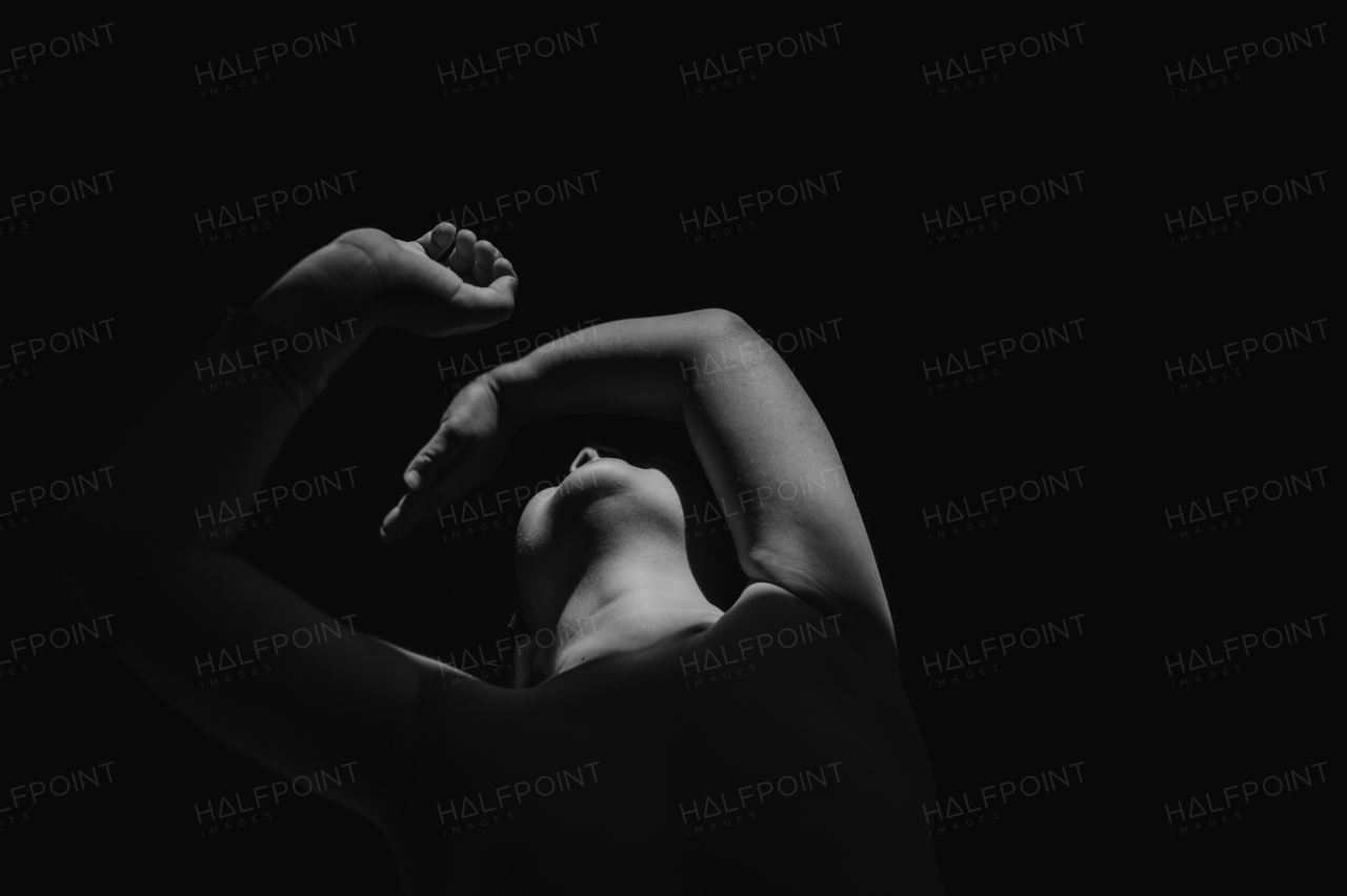 A black and white portrait of little boy raising face and covering it with hands on black background