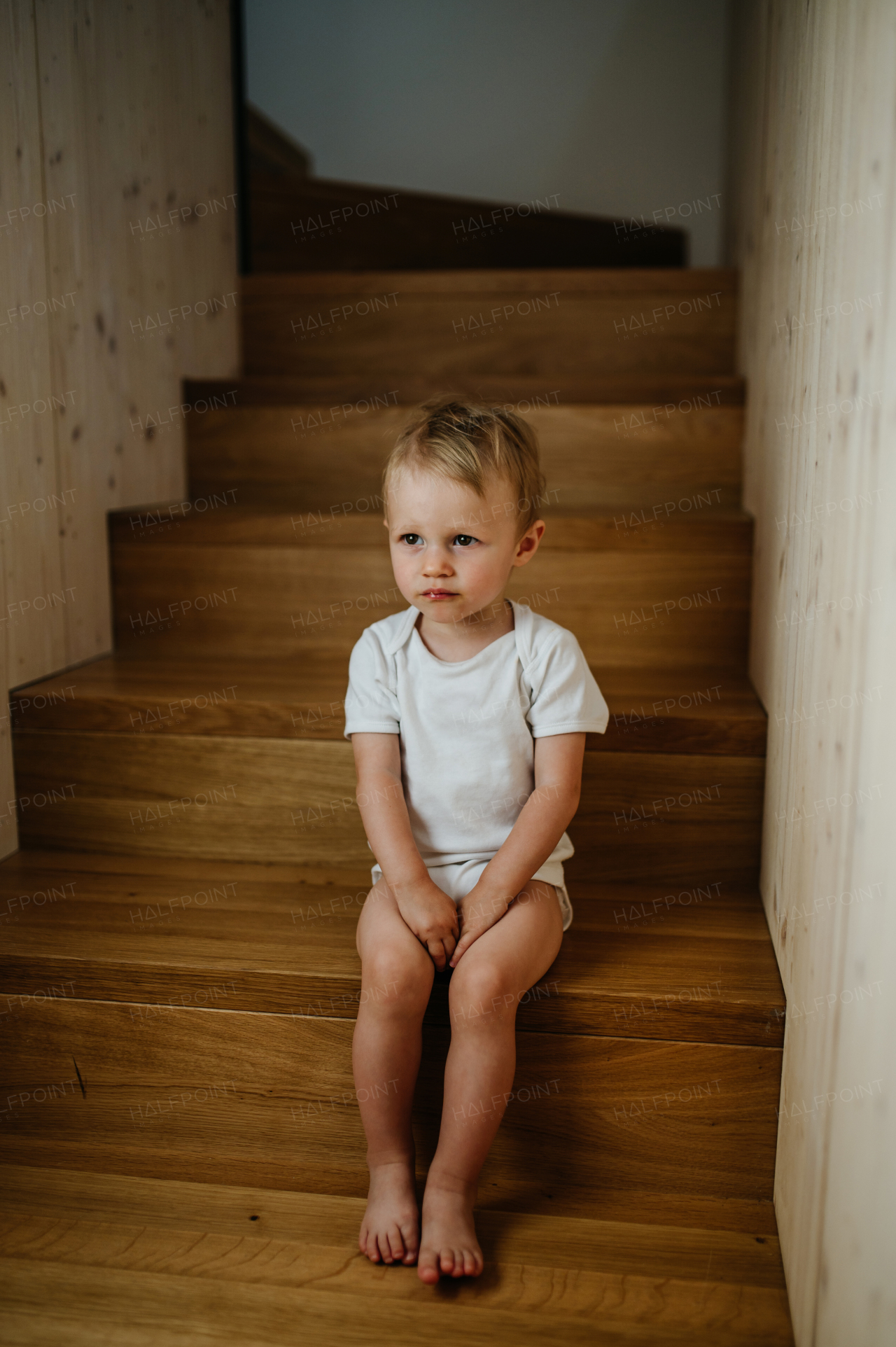 A cute little girl sitting on stairs at home and looking at camera.