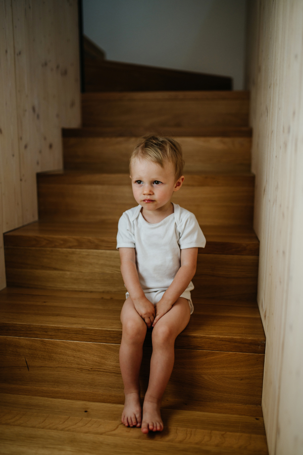 A cute little girl sitting on stairs at home and looking at camera.