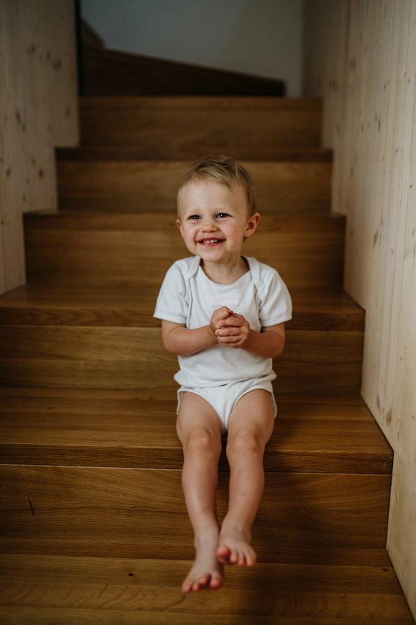 A cute little girl sitting on stairs at home and looking at camera.