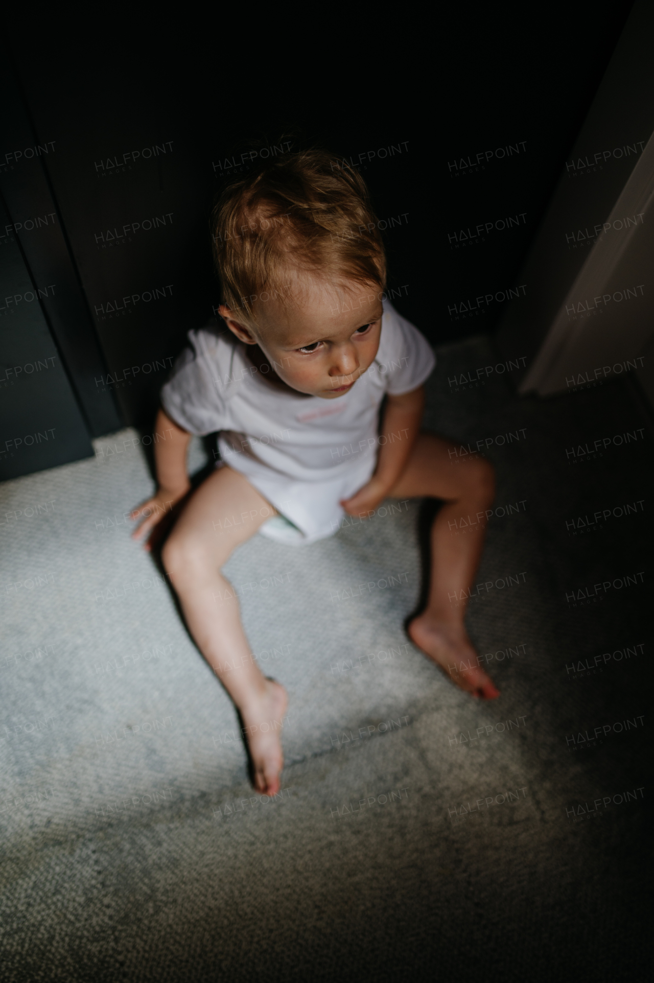 A dark high angle view portrait of sad anonymous little baby girl sitting on mfloor.