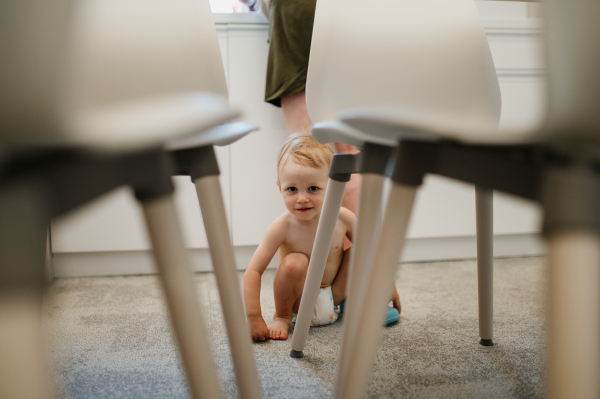 A cute toddler girl crawling takes first step, trying to stand up at home in kitchen with mother at background