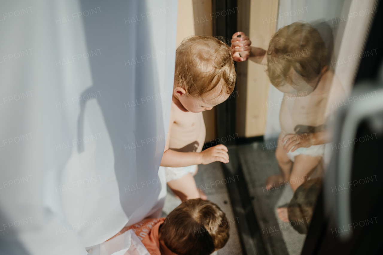 A cute baby girl playing,hiding behind curtains at home.