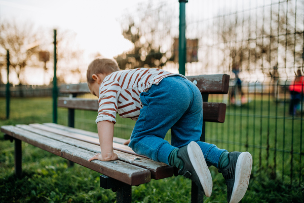 A little boy climbing up the bench on outdoor playground.