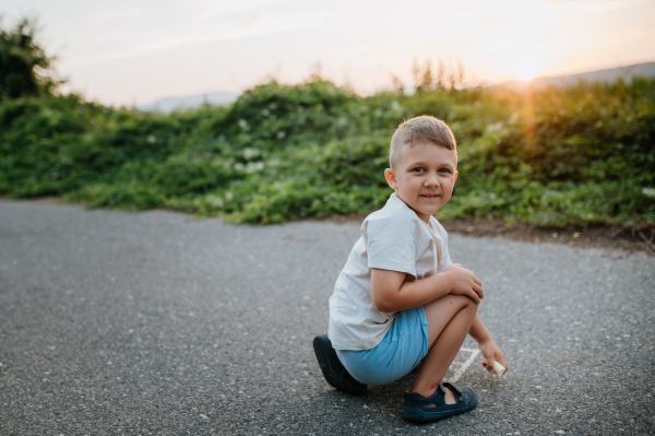 A little kid boy drawing with chalk on asphalt in summer.