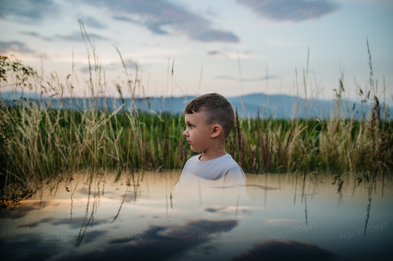 A little sad boy is standing in the field of wheat in summer.