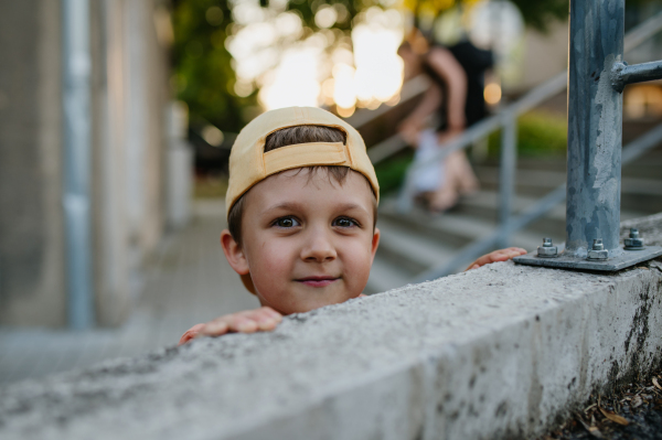 A little cute boy with looking over wall outdoors in summer