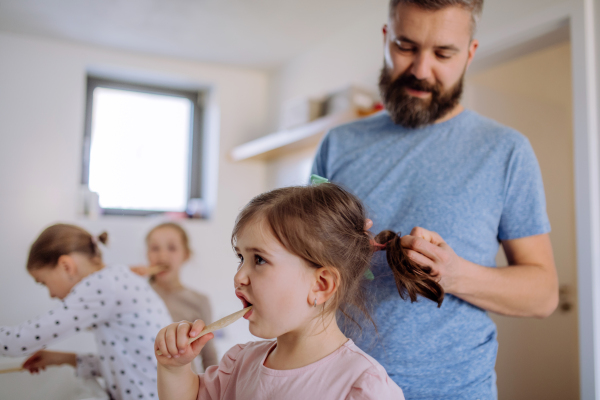 A father brushing his little daughter's hair in bathroom, morning routine concept.