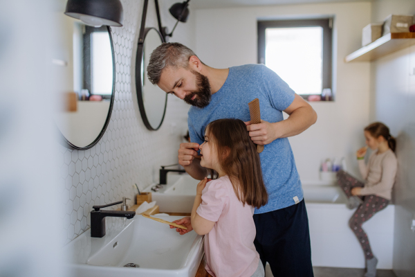 A father brushing his little daughter's hair in bathroom, morning routine concept.