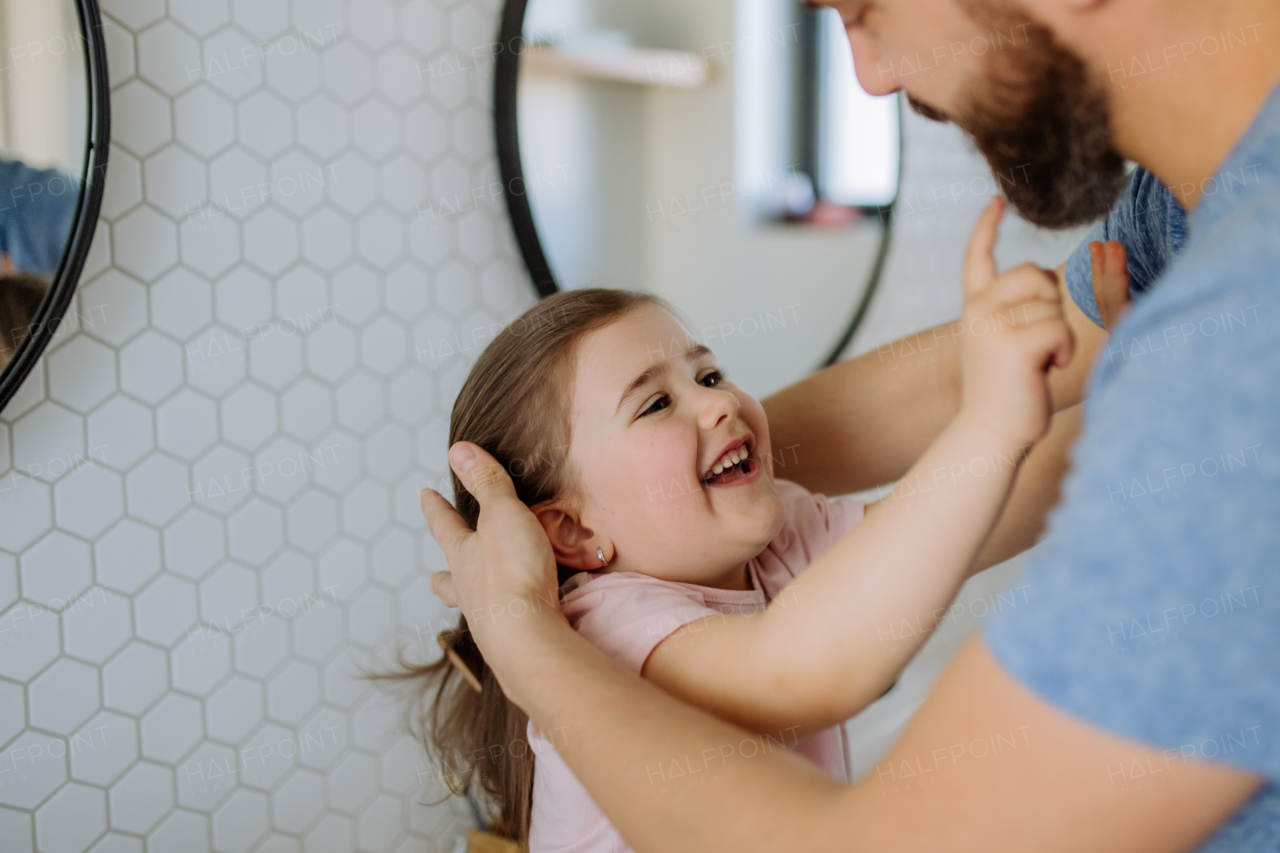 A father checking his daughter's teeth in bathroom, morning routine concept.