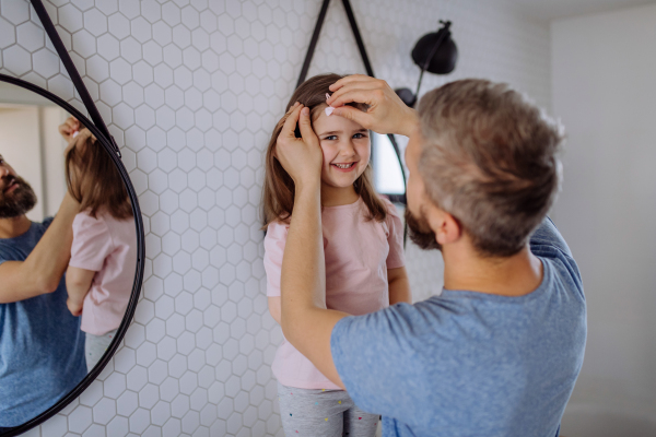 A father brushing his little daughter's hair in bathroom, morning routine concept.