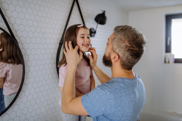 A father checking his daughter's teeth in bathroom, morning routine concept.