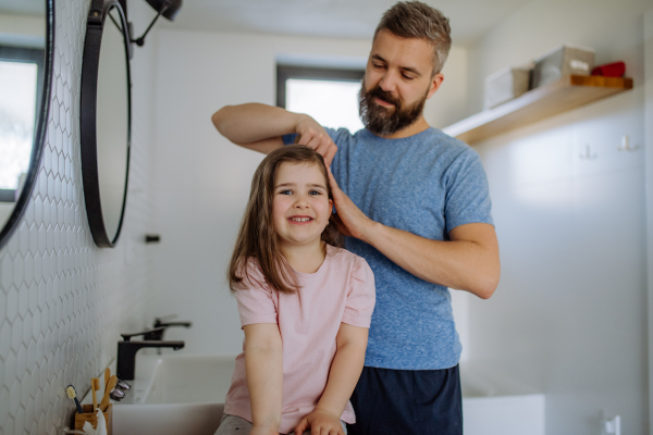 A father brushing his little daughter's hair in bathroom, morning routine concept.