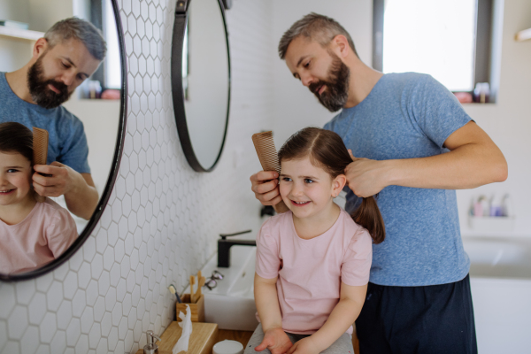 A father brushing his little daughter's hair in bathroom, morning routine concept.