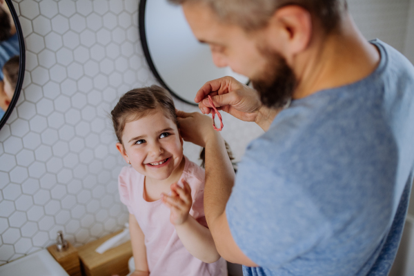 A father brushing his little daughter's hair in bathroom, morning routine concept.