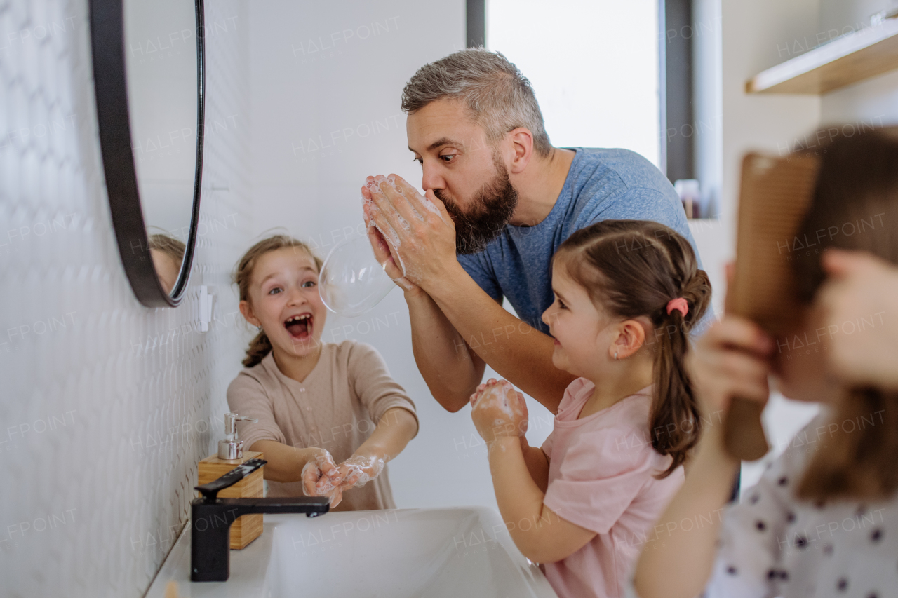 A father having fun blowing bubbles from soap in bathroom with his little daughters.