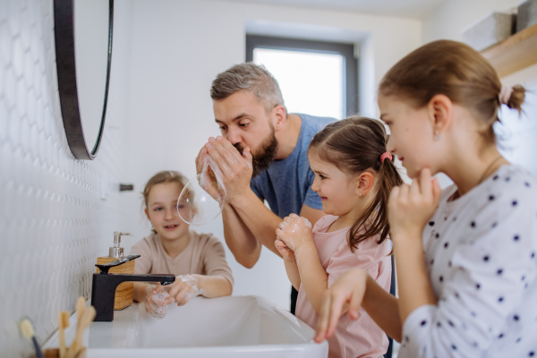 A father having fun blowing bubbles from soap in bathroom with his little daughters.