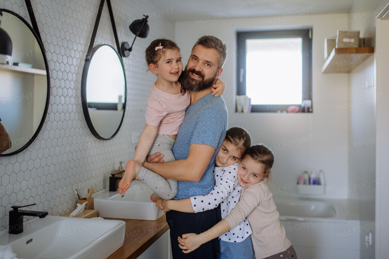 A father bonding with his three little daughters in bathroom and looking at camera.