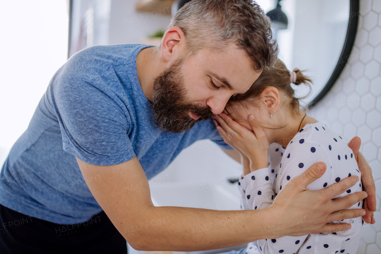 A father consoling his little upset daughter in bathroom at home.