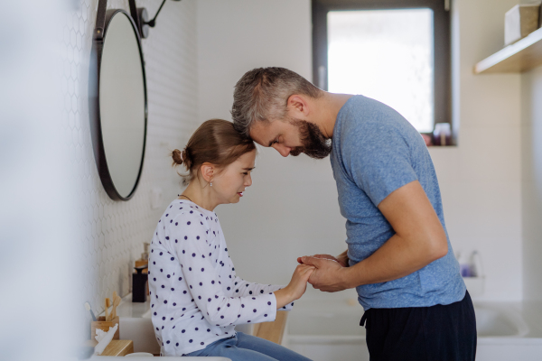 A father consoling his little upset daughter in bathroom at home.