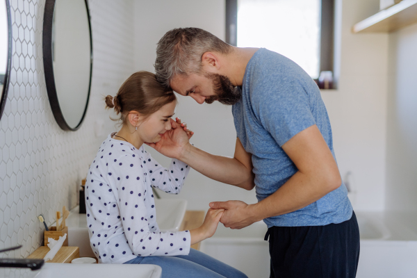 A father consoling his little upset daughter in bathroom at home.