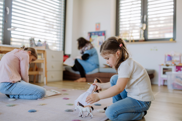 Cheerful little sisters playing together at home with toys.