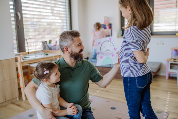 A father of three little daughters getting drawings from them at home.