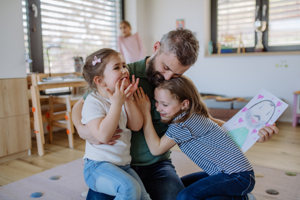 A father of three little daughters getting drawings from them at home.